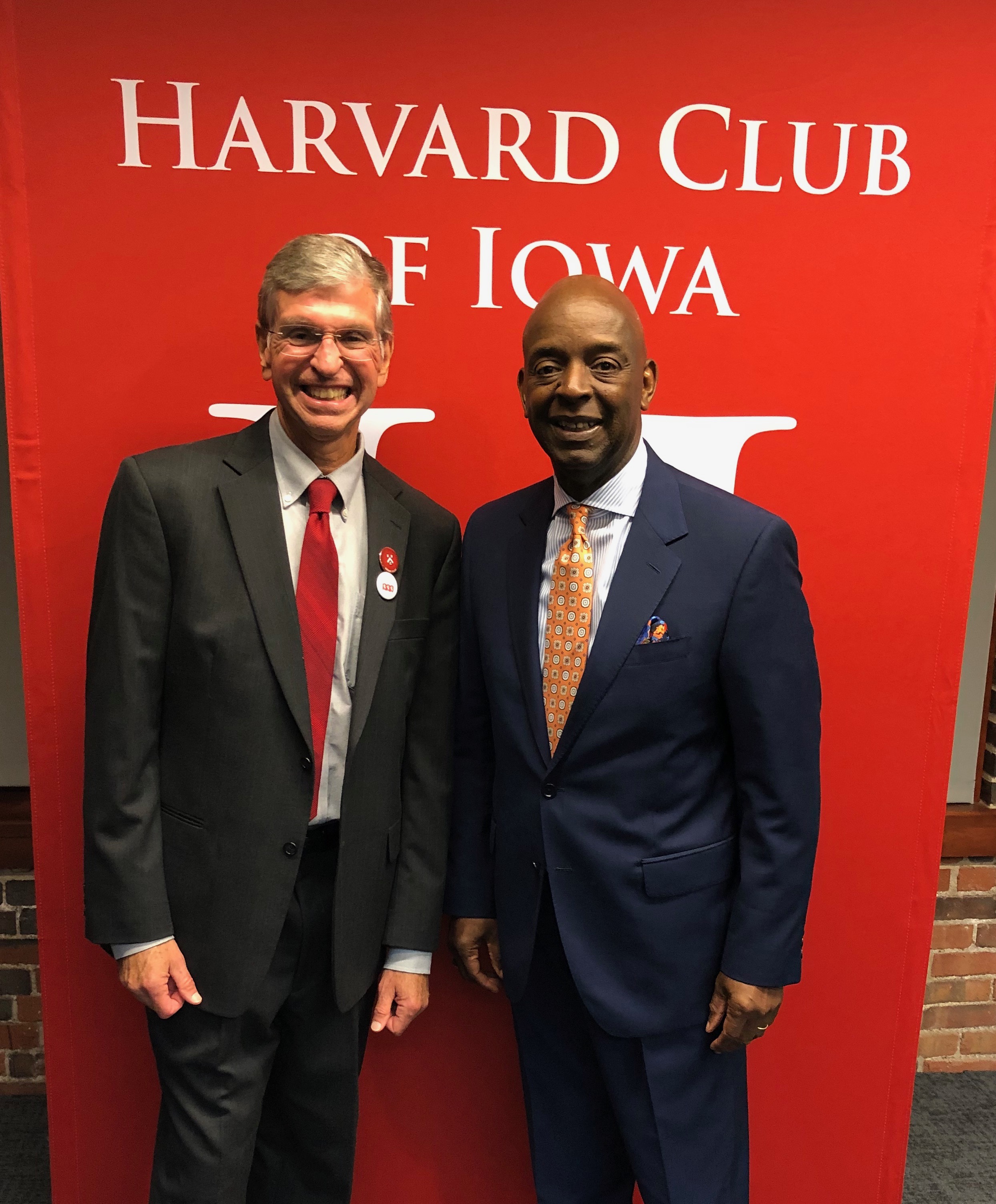 Matthew and Ronald in suits standing next to each other in front of a large red sign that reads Harvard Club of Iowa